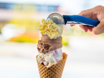 Male hand serving various flavors ice cream scoops in waffle cone