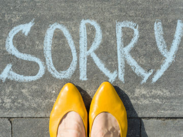 Female feet with text sorry written on asphalt