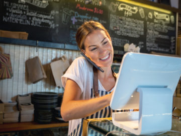 Waitress talking on the phone at a restaurant taking a delivery order and looking happy - food service concepts
