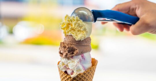 Male hand serving various flavors ice cream scoops in waffle cone