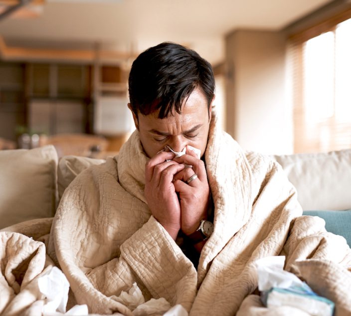 Cropped shot of a young man suffering with a cold while sitting wrapped in a blanket on the sofa at home.