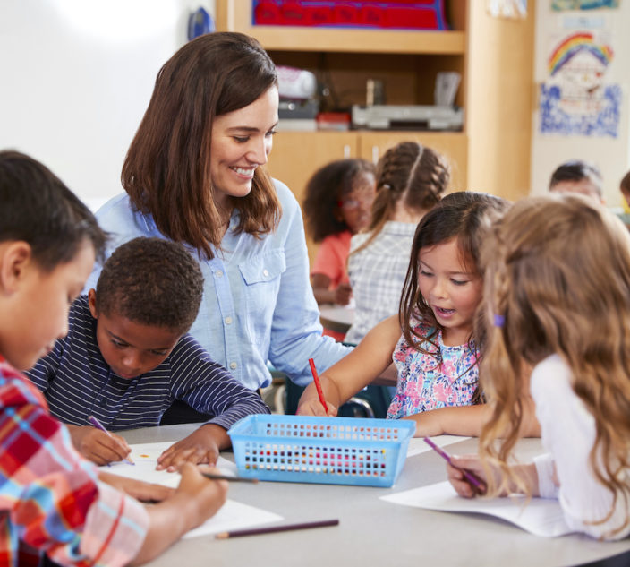 Teacher sitting at table with young school kids in lesson