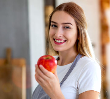 Young woman holding an apple and smiling