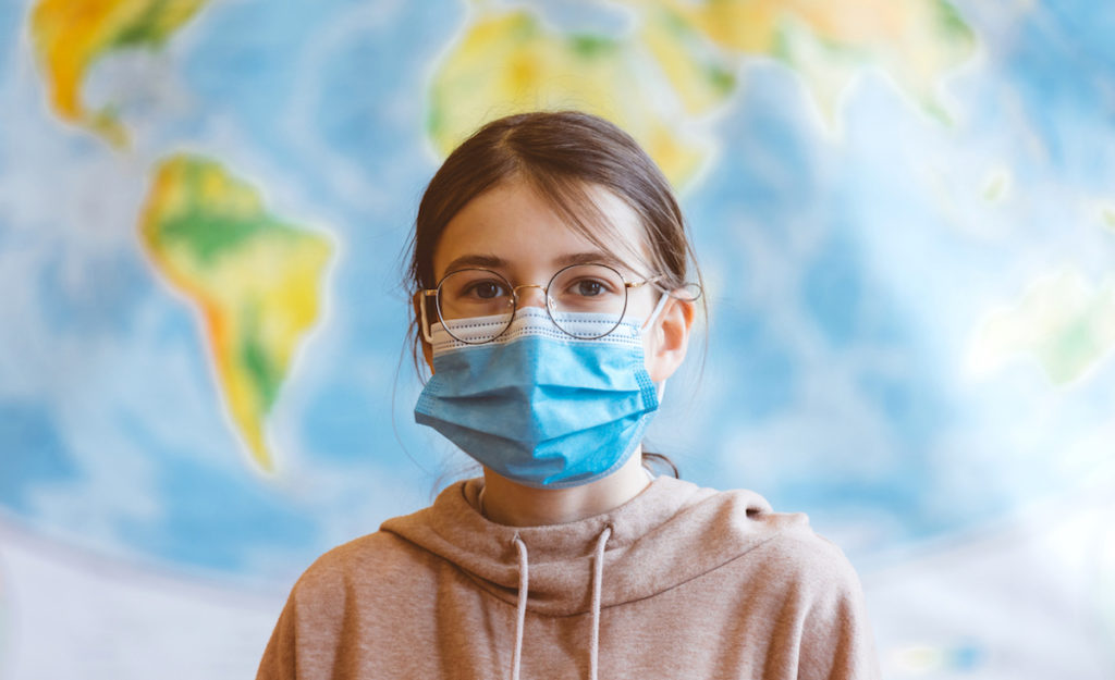 A 11-year-old teenager wearing a N95 Face masks is standing in front of a world map