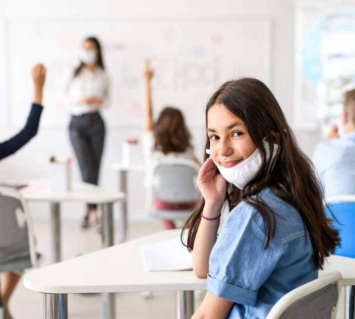 Child with face mask back at school after covid-19 quarantine and lockdown, looking at camera.