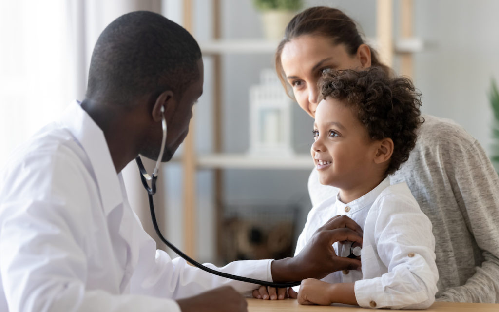 Doctor with stethoscope listening to lung and heart sound of little boy sitting on mother lap.