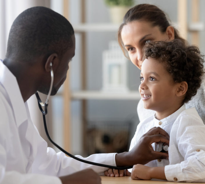 Doctor with stethoscope listening to lung and heart sound of little boy sitting on mother lap.
