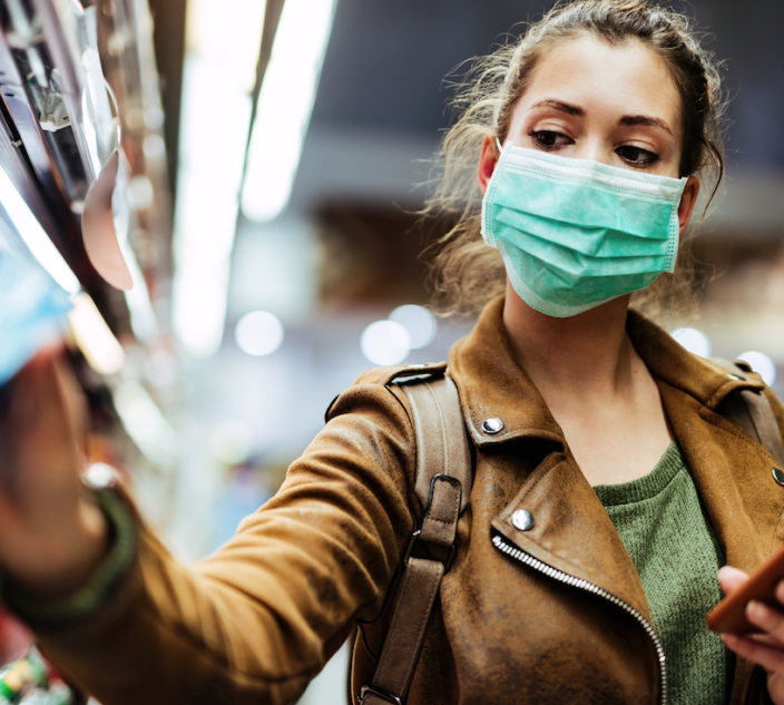 Young woman with face mask using mobile phone and buying groceries in the supermarket during virus pandemic. (Young woman with face mask using mobile phone and buying groceries in the supermarket.