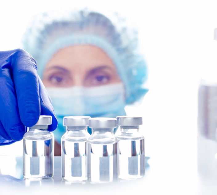 Female nurse in safety mask and gloves takes vial with liquid medicine from refrigerator shelf.