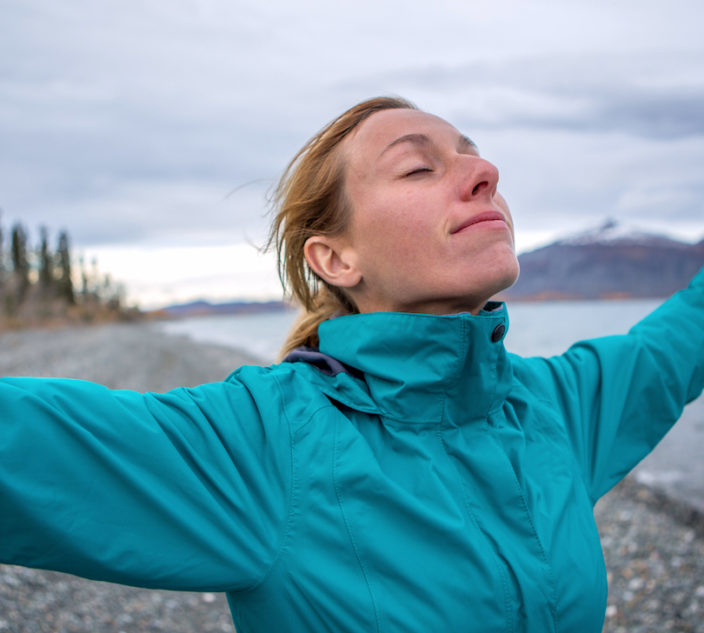 Young cheerful woman by the lake enjoying nature. Arms outstretched for positive emotion.