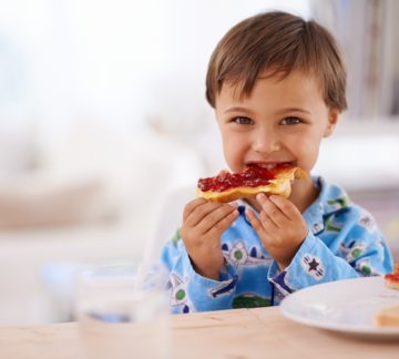 A little boy eating toast with peanut butter and jam