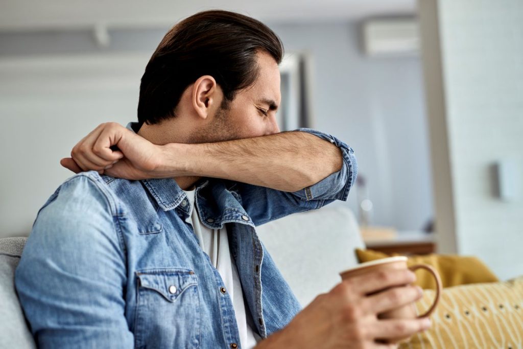 A man with asthma coughs into his arm.