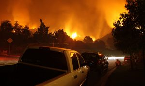 Residents of a neighborhood sit by and watch a fire threaten their homes.