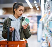 Young woman reading food label in grocery store.