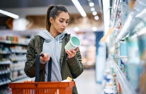 Young woman buying diary product and reading food label in grocery store.