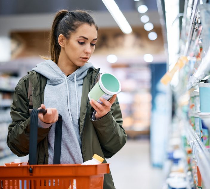 Young woman buying diary product and reading food label in grocery store.