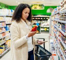 A woman standing in an isle in her local supermarket and reading the product label of an item while out grocery shopping.